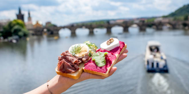 Hand holding must-try foods in Prague, with the river on the background.