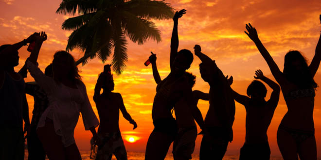 Silhouettes of people partying on a Caribbean beach with Stripe, the best Jamaican beer.