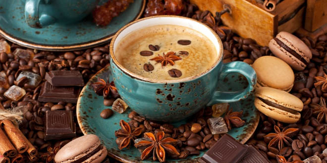 Coffe cup over coffee beans, spices, chocolate and other coffee foods.