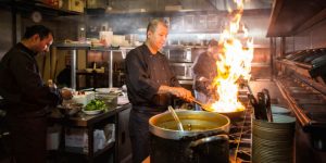 Three Asian chefs cooking some national dishes from all over the world in a restaurant kitchen.