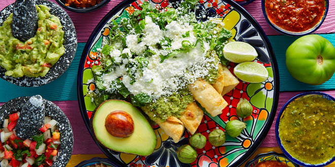 Buy international foods. Mexican green enchiladas with guacamole and sauces on colorful table.