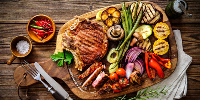 Grilled beef steak with grilled vegetables on serving board block after being prepared on cooking grills.